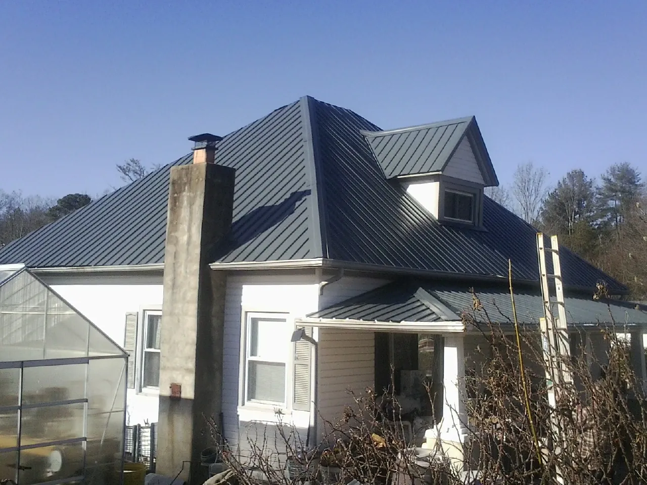 Dark blue standing seam metal roof on a white farmhouse with dormer — Slate & Tile Roof Repair by Roofing Brothers in Eagle Grove