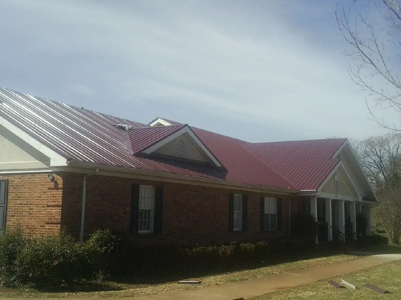 Red metal roof with gabled entries on a long brick building, from a Hail Damage Roof Repair job in Eagle Grove