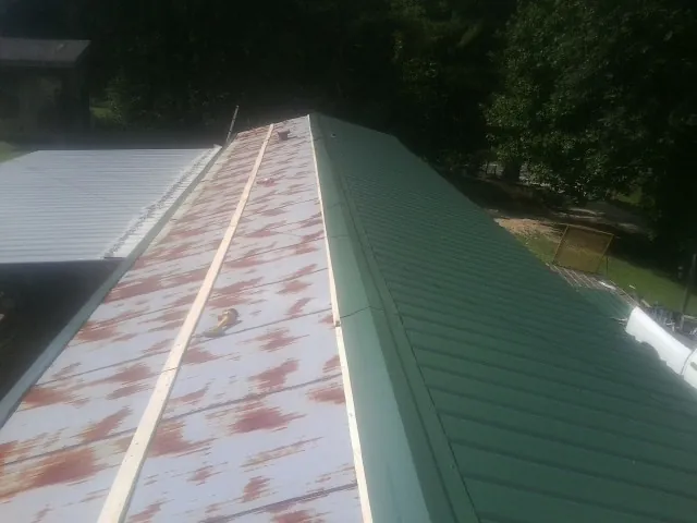 Old rusted panels beside newly installed green metal roofing — Wind Damage Roof Repair by Roofing Brothers in Eagle Grove