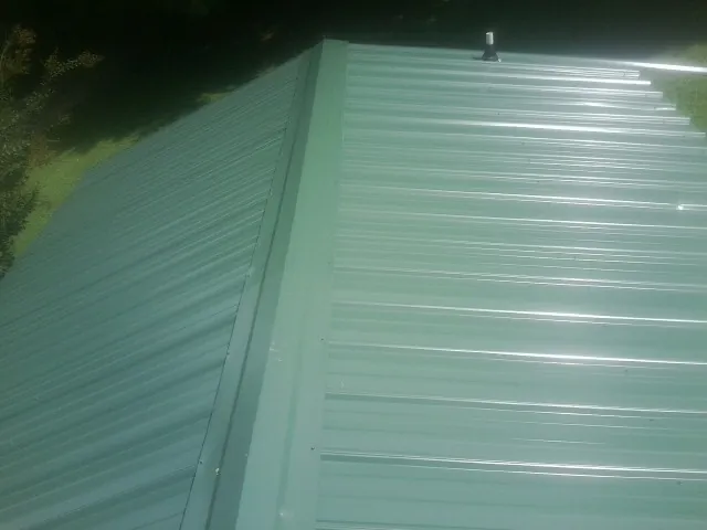 New green metal panels meeting at the ridge of a roof — Flat Roof Repair work by our crew in Eagle Grove