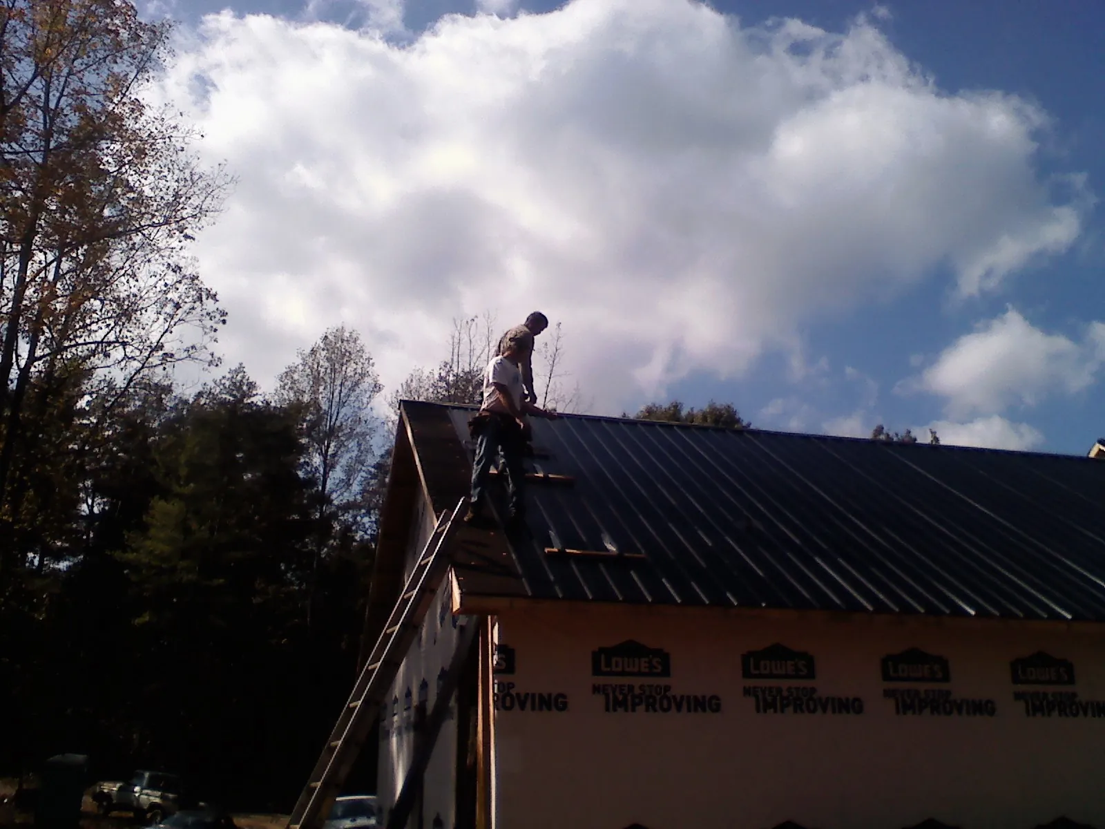 Roofer fastening dark metal panels high against a cloudy sky, from a Roof Inspection job in Eagle Grove