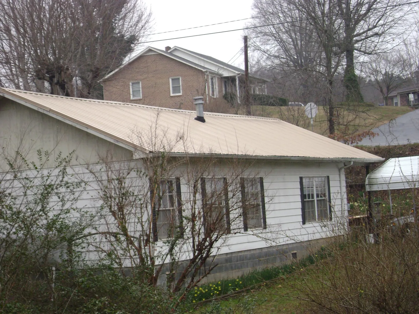 Tan metal roof on a white sided house set into a hillside — Commercial Roofing by Roofing Brothers in Eagle Grove