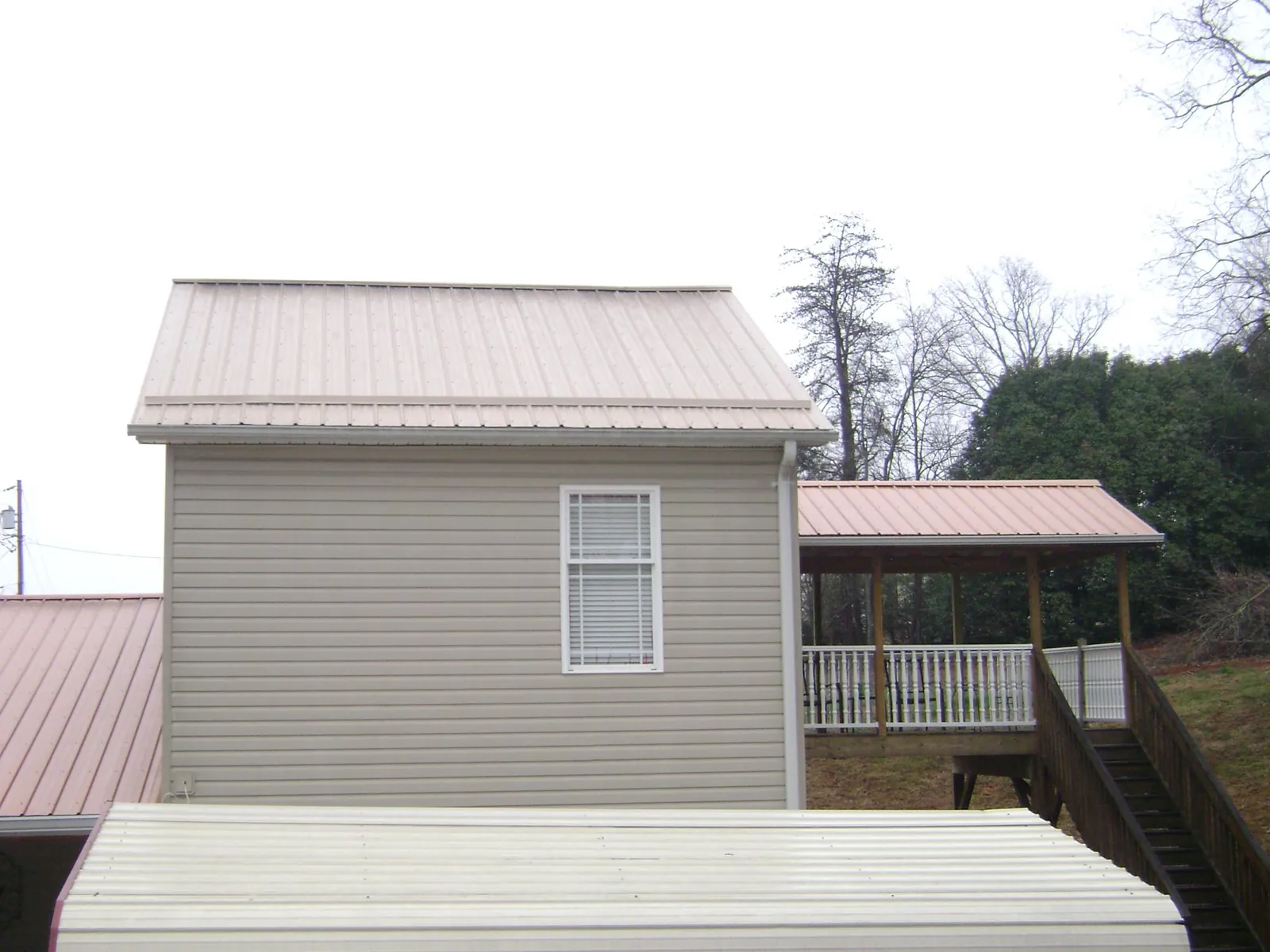 Tan metal roofs on a two story addition and attached porch, from a Roof Replacement job in Eagle Grove
